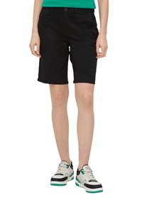 Svarta shorts i bomull, med slät framsida, fickor och bältesöglor. Kombinerat med vita och svarta sneakers med gröna accenter.