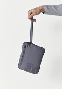 Szara, wyściełana saszetka z zamkiem błyskawicznym, trzymana w dłoni. Posiada pętelkę na uchwycie oraz subtelnie tłoczone logo z przodu. Gładka tekstura.