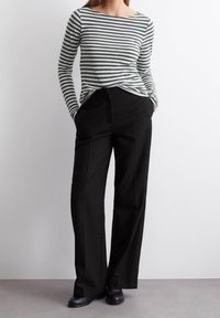 Gestreepte lange mouwen top in groen en grijs, gecombineerd met hoge taille zwarte broek. De outfit heeft een relaxte pasvorm en voorzakken.
