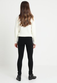 Vit ribbad tröja, svarta smala jeans och ankelstövlar. Tröjan har en avslappnad passform och jeansen har bakfickor.