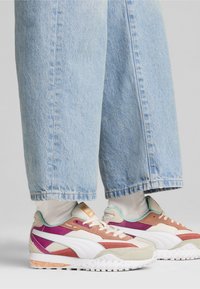 Le sneakers colorate presentano una combinazione di beige, viola e accenti menta con una suola testurizzata. Abbinati a jeans a gamba larga di un blu chiaro.