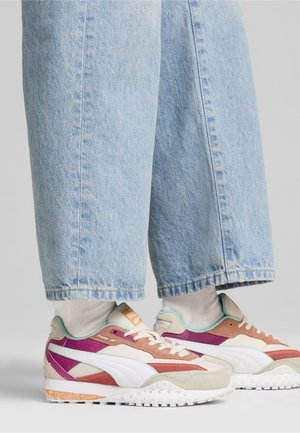 Des baskets colorées présentent un mélange d'accents beige, violet et menthe avec une semelle texturée. Associées à un jean large bleu clair.