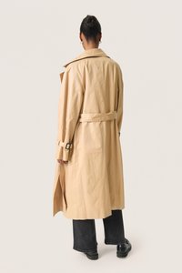Beige trenchcoat med bælte i taljen, stort krave og spænde detaljer. Har en let tekstureret overflade, afklippede ærmer og slids bagpå.