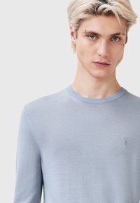 Maglione azzurro chiaro a girocollo realizzato in materiale morbido. Presenta maniche lunghe e dettagli di cucitura sottili, con un piccolo logo sul petto.