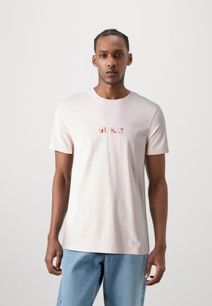 T-shirt di cotone rosa chiaro con scollo a girocollo, maniche corte e logo ricamato "GUESS" in colori sfumati sul petto.