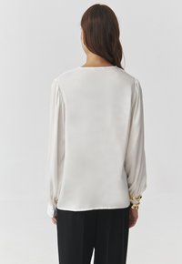 White long-sleeve blouse with a relaxed fit, featuring a slightly rounded neckline and gathered sleeves. Smooth, satin-like texture.