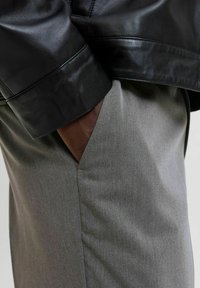 Black leather jacket sleeve rests over gray pants with a subtle texture. The pants feature a side pocket, showcasing a sharp, clean design.