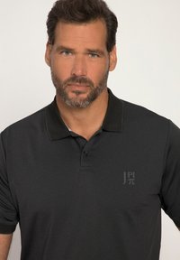 Sort polo-shirt lavet af glat stof, med krave, to knapper og et diskret logo på brystet.