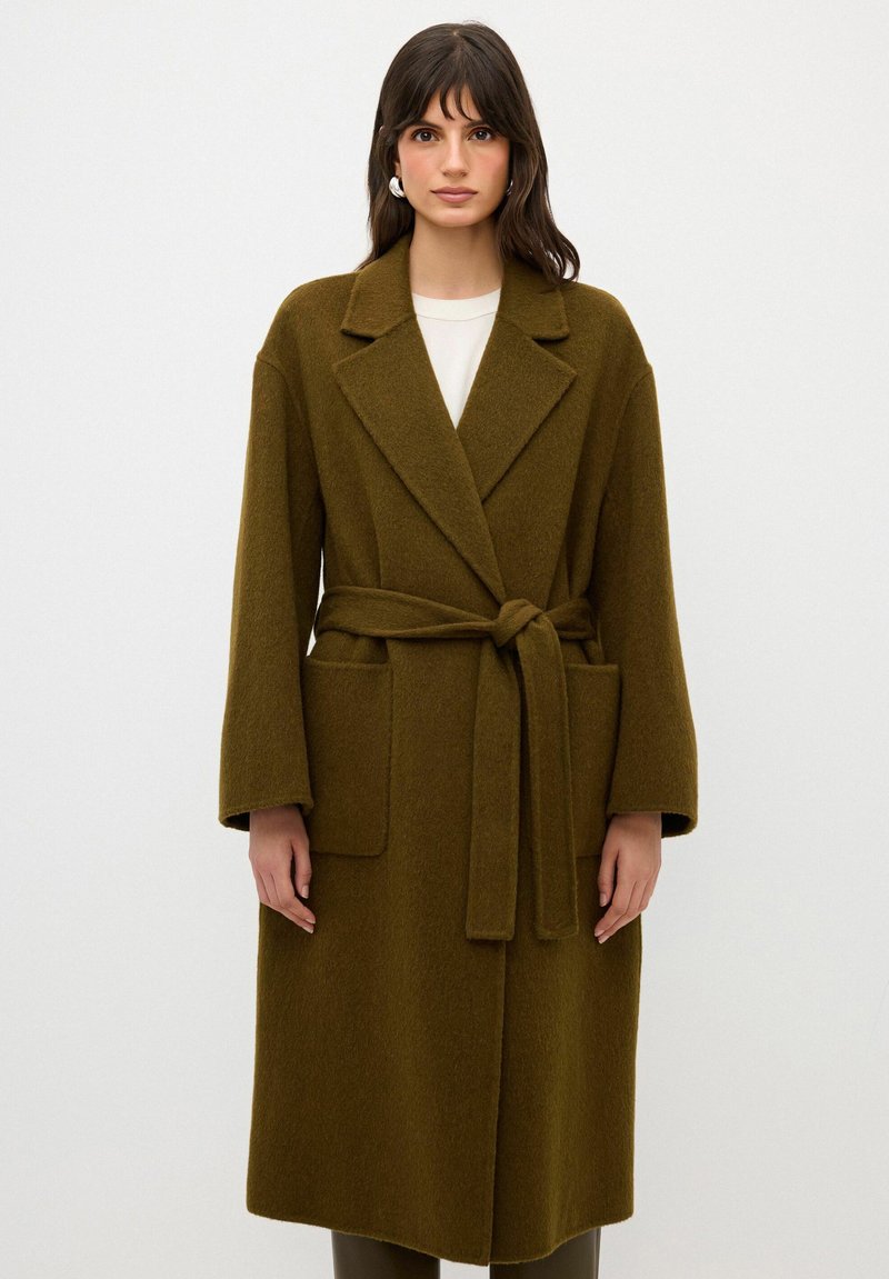 Olivgrön, ullblandad kappa med bälte, breda slag, långa ärmar och två framfickor. Mjukt material och knälång design.
