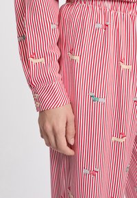 Rood-wit gestreepte stof met geborduurde teckels die truien dragen. Het shirt heeft knoopmanchetten en een ontspannen pasvorm.