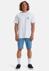 Witte t-shirt met een rond logo op de borst, gecombineerd met lichtblauwe shorts, witte sokken en donkerblauwe schoenen. Eenvoudig ontwerp, casual pasvorm.