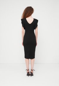 Μαύρο στενό φόρεμα με V-πλάτη, φουσκωτά μανίκια, μήκος μέχρι το γόνατο και σκίσιμο στην πλάτη. Φορεμένο με μαύρες ψηλοτάκουνα σανδάλια με λουράκια.