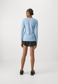 Light blue long-sleeve shirt, fitted, with a crew neckline, paired with black shorts and black sneakers; smooth texture with minimal design details.