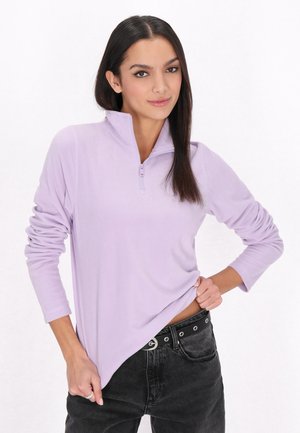 Hellpurpurfarbenes Viertel-Reißverschluss-Pullover aus weichem Fleece-Stoff, mit langen Ärmeln und lockerer Passform. Kombiniert mit schwarzen Jeans.