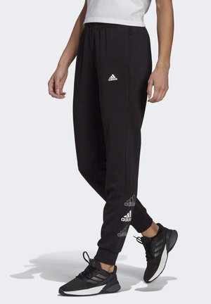 Zwarte adidas joggers met een slim fit, elastische tailleband en logo-accenten aan de zijkanten. Gecombineerd met zwarte sportschoenen.