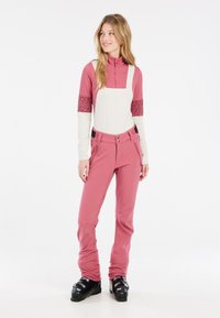 Ružový lyžiarsky outfit s topom na zips a bielym predným panelom a vzorovanými rukávmi. Zodpovedajúce ružové lyžiarske nohavice s bočnými zipsami a gombíkmi.