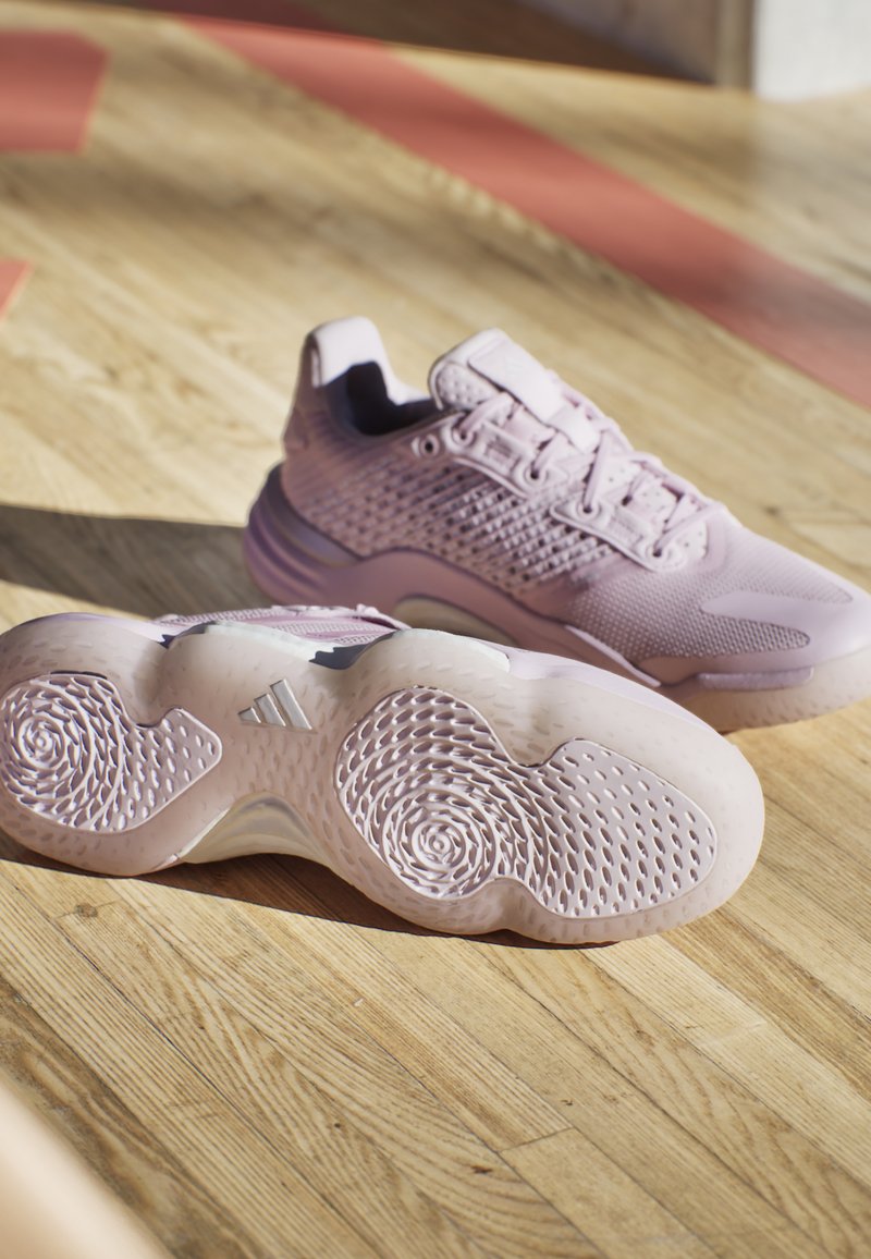 Zapatillas deportivas de color rosa claro con una parte superior de malla texturizada, suelas acolchadas y una suela exterior de patrón detallado. Mayor agarre con patrones redondos.