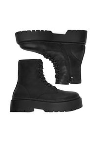 Para czarnych skórzanych butów typu lace-up z grubą, żłobioną podeszwą i bocznymi zamkami, wyeksponowanych na białym tle.