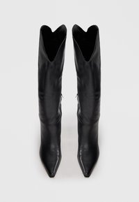 Bottines en cuir noir avec un bout pointu et une ouverture en V sur le dessus. Texture lisse et design épuré, créant une silhouette élancée.