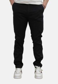 Zwarte slim-fit broek met een gladde textuur, voorzien van zijzakken en een eenvoudig ontwerp, gecombineerd met zwart-witte sneakers.