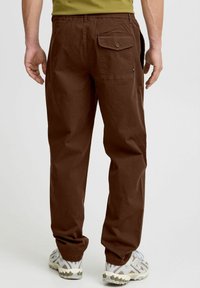 Braune, lässige Cargo-Hosen mit einem Gesäßtasche und elastischem Bund. Getragen mit hellen, strukturierten Sportschuhen.