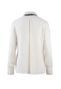 Blusa bianca a maniche lunghe con colletto, caratterizzata da un design con schiena aperta e un accento nero lungo il collo. Tessuto morbido e vestibilità sartoriale.