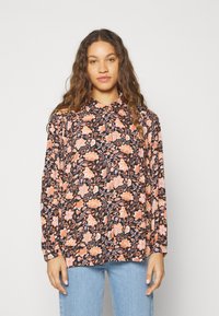 Blusa de manga larga floral con base negra, que presenta flores en tonos rosa y naranja, cuello abotonado y mangas con fruncido. Combinada con jeans de un suave tono azul.