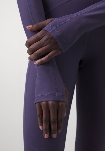 Fialová športová blúzka s otvorom na palce a predĺženými manžetami. Hladká štruktúra s viditeľným švom a tesným strihom okolo rúk.