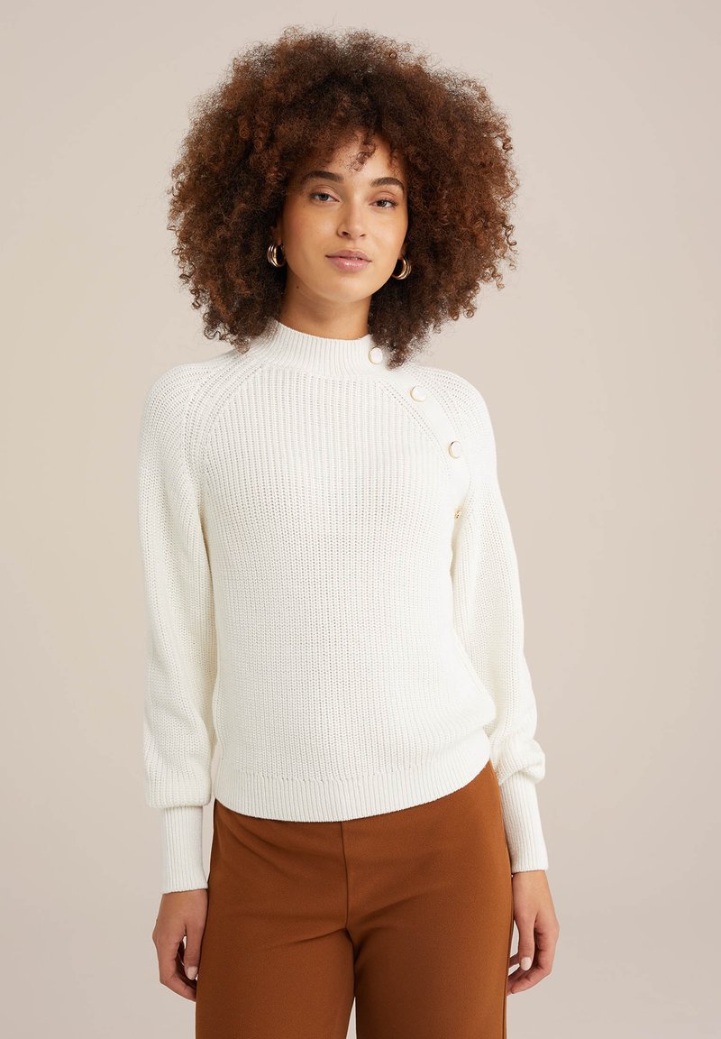 Baltas megztinis su aukšta apykakle, raukšlėtais rankogaliais ir prigludusia apatine dalimi. Kairėje peties pusėje yra dekoro mygtukai. Lygus paviršius.