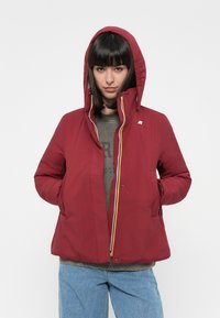 Rote isolierte Jacke mit Kapuze, seitlichen Taschen und einem Frontreißverschluss mit gelben Akzenten. Das Material wirkt glatt und leicht glänzend.