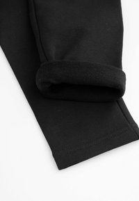 Czarne bawełniane spodnie z miękkim, podwiniętym mankietem i gładką teksturą, z widocznym szwem wzdłuż boku.