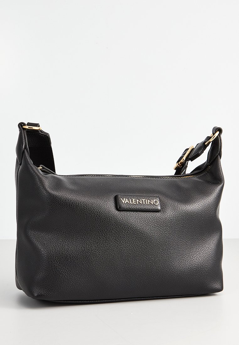 Bolso de hombro de cuero negro con un acabado texturizado, que presenta un detalle en oro y una placa de marca en la parte frontal. Correa ajustable.