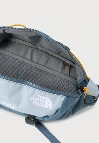 Μπλε και γαλάζια τσάντα μέσης με φερμουάρ, εσωτερική τσέπη από δίχτυ, κίτρινη ταινία φερμουάρ, ρυθμιζόμενο λουράκι και ορατό το λογότυπο The North Face.