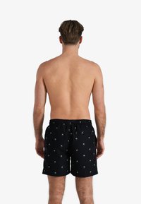 Zwarte zwembroek met een groen palmboompatroon, gemaakt van lichtgewicht materiaal, met een elastische tailleband en een achterzak.