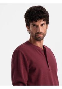 Burgundská dlouhá halenka henley s texturovanou tkaninou, s mírně otevřeným límcem a jedním knoflíkem.