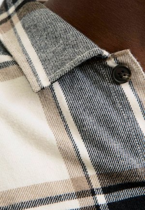 Plaid shirt featuring beige, black, and white colors with a textured fabric. Includes a collar and a black button on the neck area.