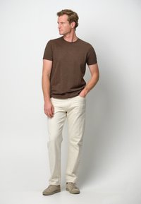 T-shirt marrone a maniche corte abbinato a pantaloni leggeri bianchi e sneakers beige. Tessuto visibile e vestibilità casual.