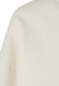 Krémové tričko s jemnou rebrovanou textúrou. Disponuje voľným strihom a krátkymi rukávmi. Bez viditeľných vzorov alebo hardvérových detailov.