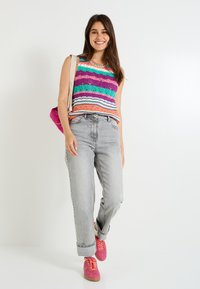 Top sin mangas de punto colorido con rayas en púrpura, turquesa y naranja, combinado con jeans gris claro y zapatillas rosas. Look casual con accesorios.