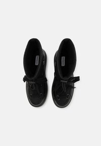 Black high-top shoes with a smooth outer material, featuring a lace-up design, padded collar, and metal accents. Textured interior lining.
