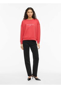 Czerwona bluza z napisem „imagine” białą kursywą, luźny fason, ściągacze na rękawach, w połączeniu z czarnymi spodniami o prostych nogawkach i czarnymi butami na obcasie.