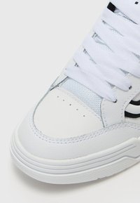 Sneaker en cuir blanc avec une surface texturée, ornée d'accents bleus, de rayures noires et de lacets blancs plats. Bout arrondi et semelle à motifs.