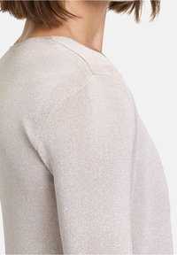 Ljus beige stickad tröja med en subtil lyster, med rundad halsringning och åtsittande ärmar. Texturen �är slät med ribbdetaljer.