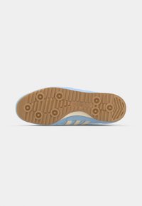 Suela de zapato deportivo de color azul claro con un patrón de tracción de goma, que presenta tres rayas beige a lo largo del lado superior y detalles texturizados.
