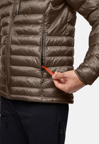 Giacca puffa marrone con cuciture orizzontali, dotata di tasca laterale con zip e un vivace tirante rosso etichettato "PACK AWAY."