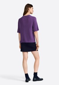 Purple short-sleeve sweater made from knitted fabric, featuring a relaxed fit and ribbed hem, paired with a navy mini skirt and black shoes.