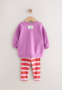 Paarse katoenen trui met een label op de achterkant. Gecombineerd met rood-wit gestreepte legging met een gerimpelde zoom.