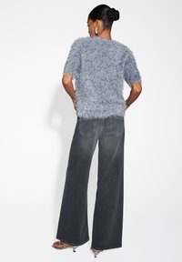 Fuzzy blue short-sleeve sweater with a loose fit, paired with high-waisted, wide-leg dark jeans and silver strappy heels.