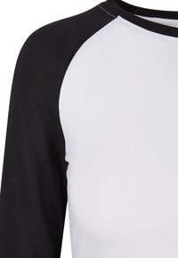 Raglanærmet skjorte i hvid og sort bomuldsblanding. Har rund hals, kontrastfarvede ærmer og en glat tekstur.