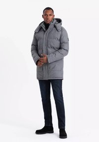 Cappotto isolato grigio con cappuccio, caratterizzato da un tessuto testurizzato, bottoni a pressione e tasche laterali. Abbinato a jeans scuri e stivali neri.